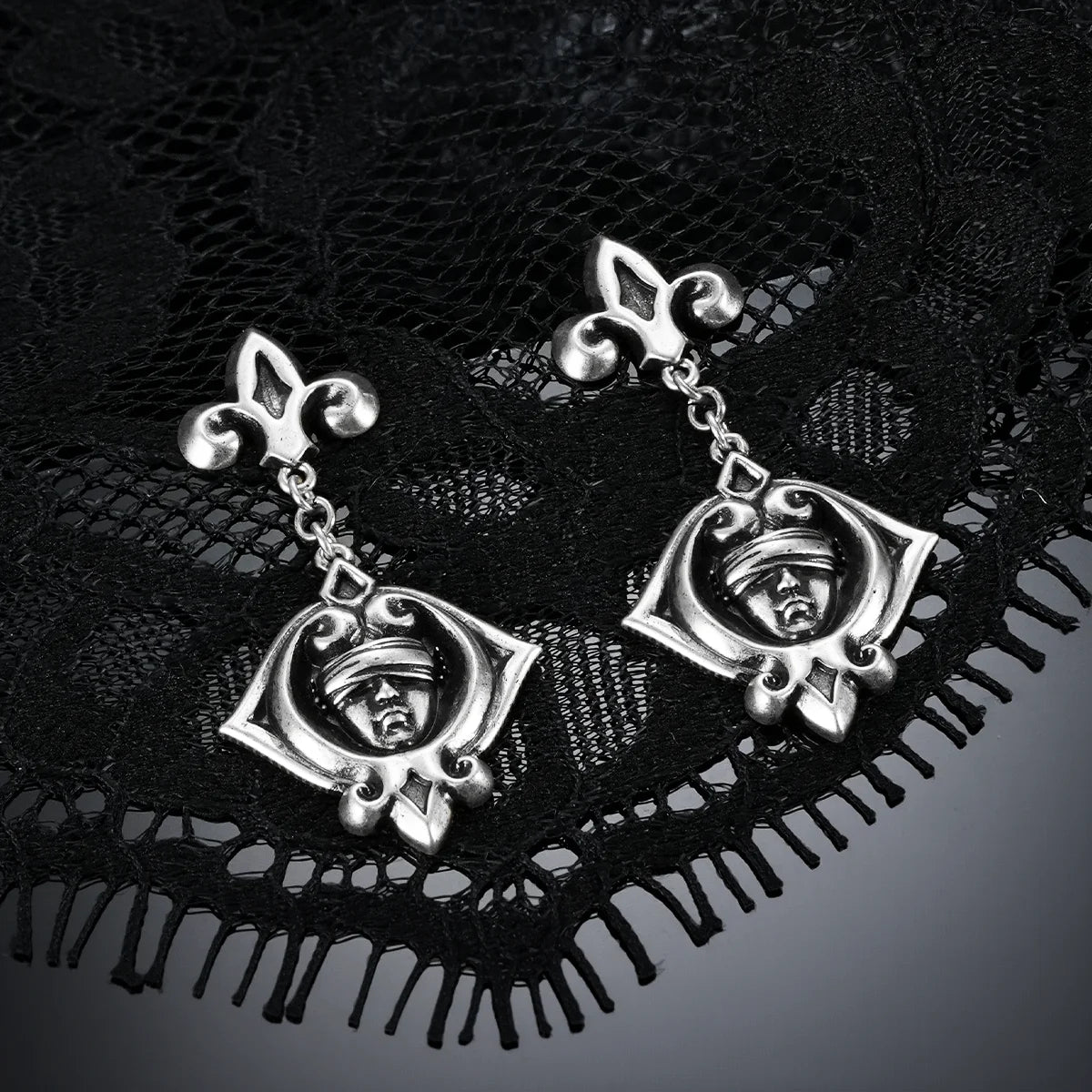 Antiqued silver-tone Veiled Seer Drop Earrings displayed as a pair against black lace on a dark reflective surface.
