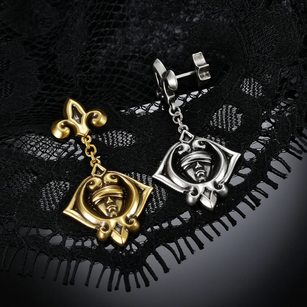 Antiqued silver- and gold-tone Veiled Seer Drop Earrings displayed together against black lace on a dark reflective surface.