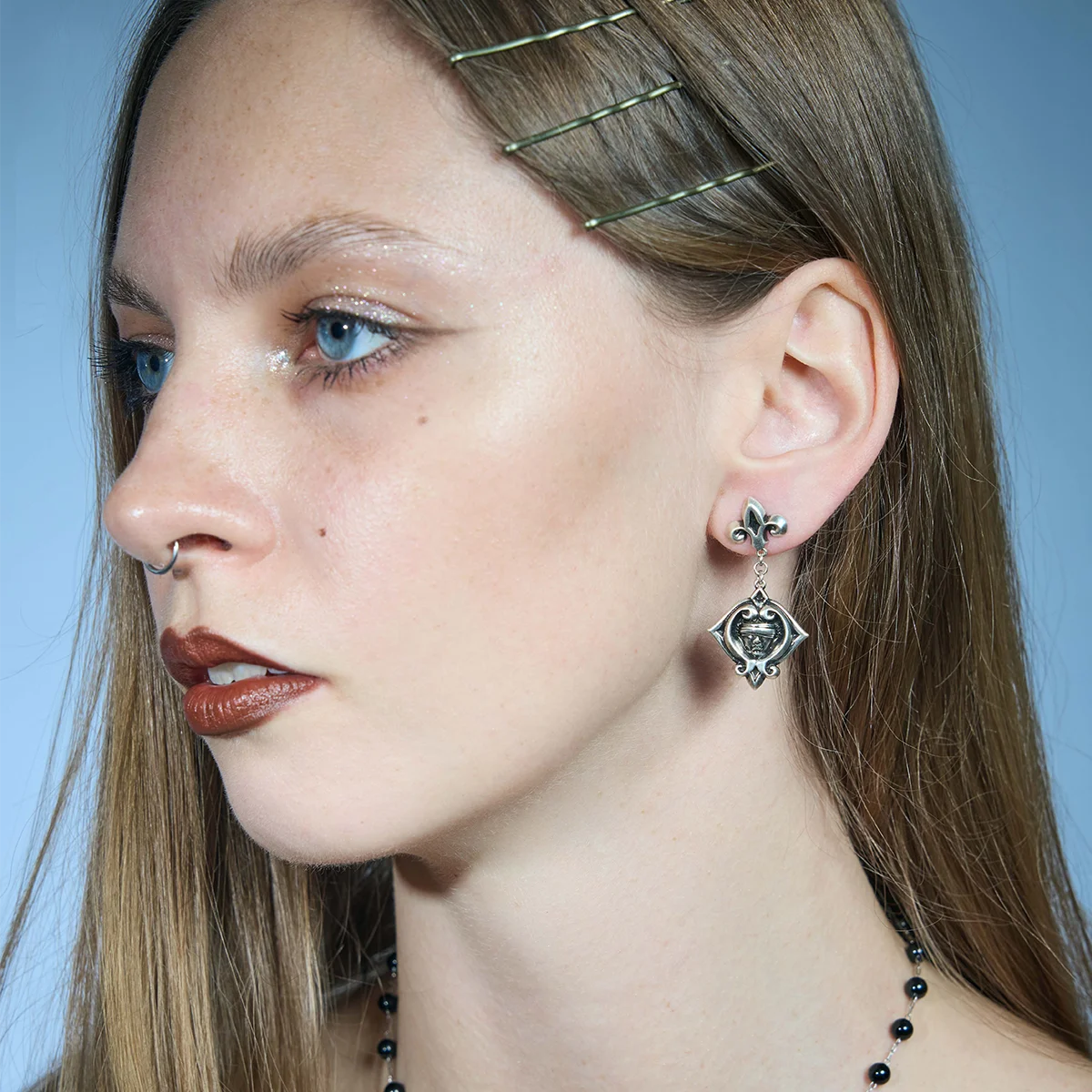 Three-quarter portrait showing antiqued silver-tone Veiled Seer Drop Earrings with blindfolded face medallions.