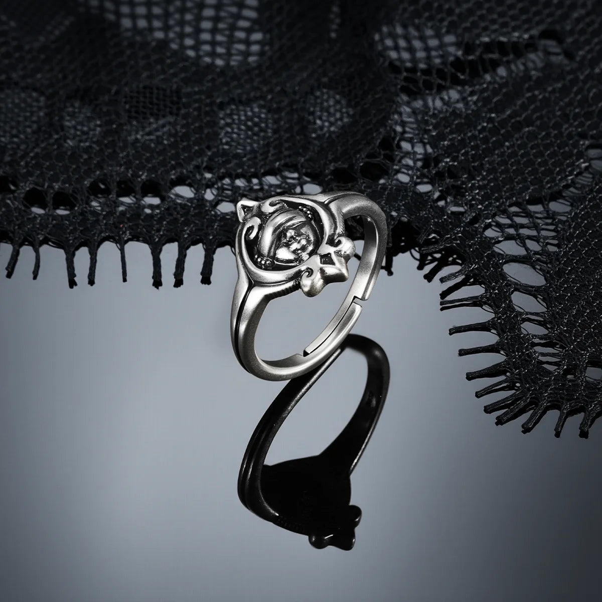 Antiqued silver Veiled Seer Ring displayed from the side on a dark reflective surface, showing the open band and raised centerpiece.