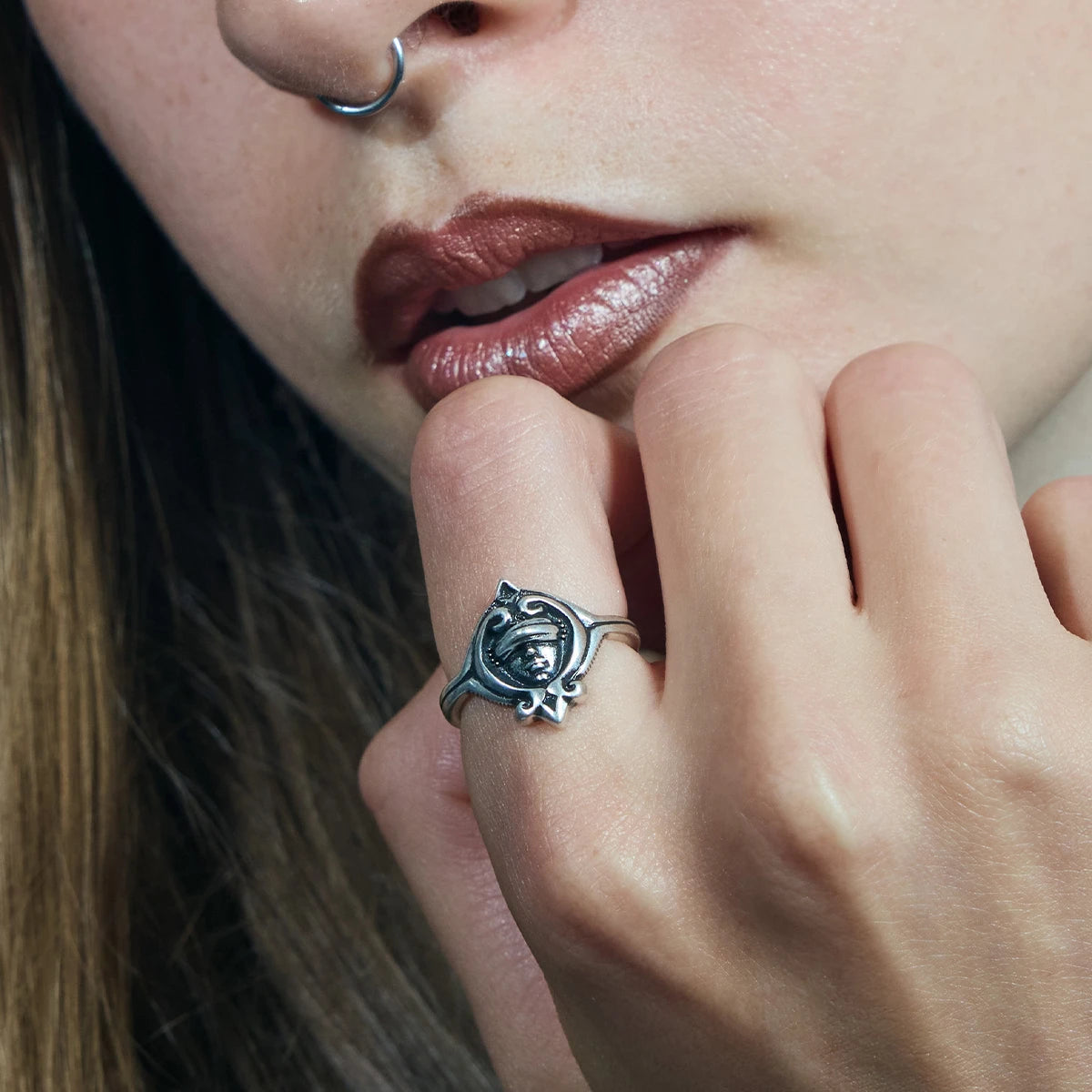 Close-up of an antiqued silver Veiled Seer Ring worn with the hand raised near the chin, showing the sculpted face motif.