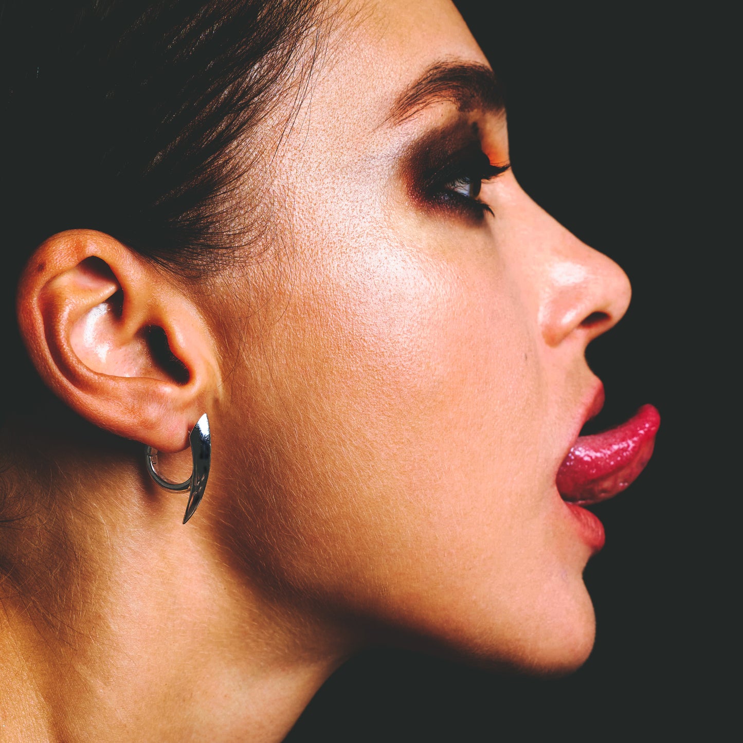 Close profile view of a model wearing a silver claw hoop earring on the ear