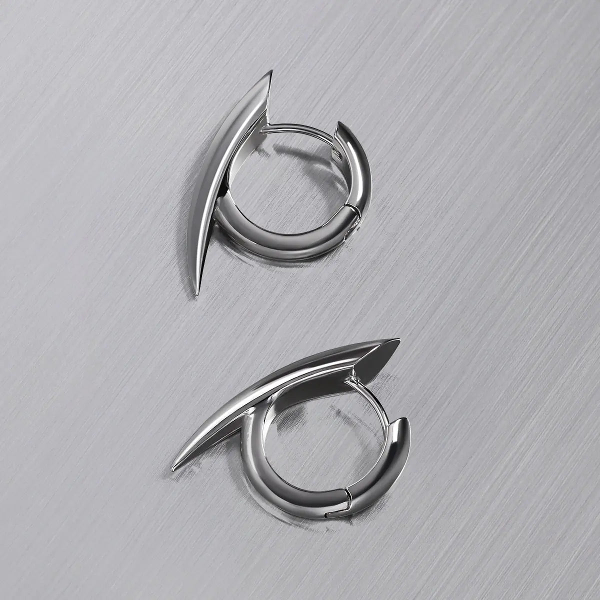 Venom Claw Earrings in 925 sterling silver, pair arranged on brushed metal to show the curved claw form from above.