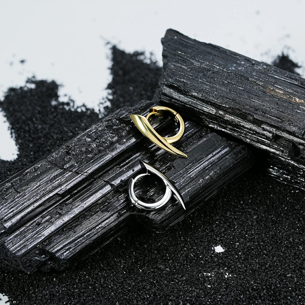 Silver and gold Venom Claw hoop earrings displayed on black crystal