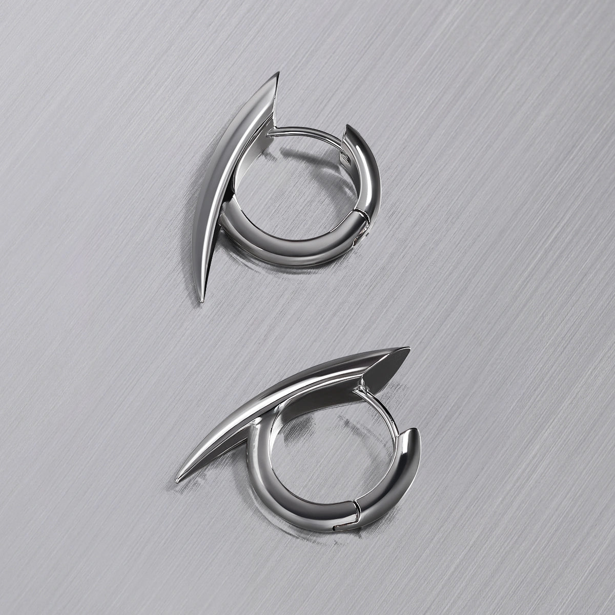 Pair of silver-tone claw hoop earrings laid flat on a brushed metal surface