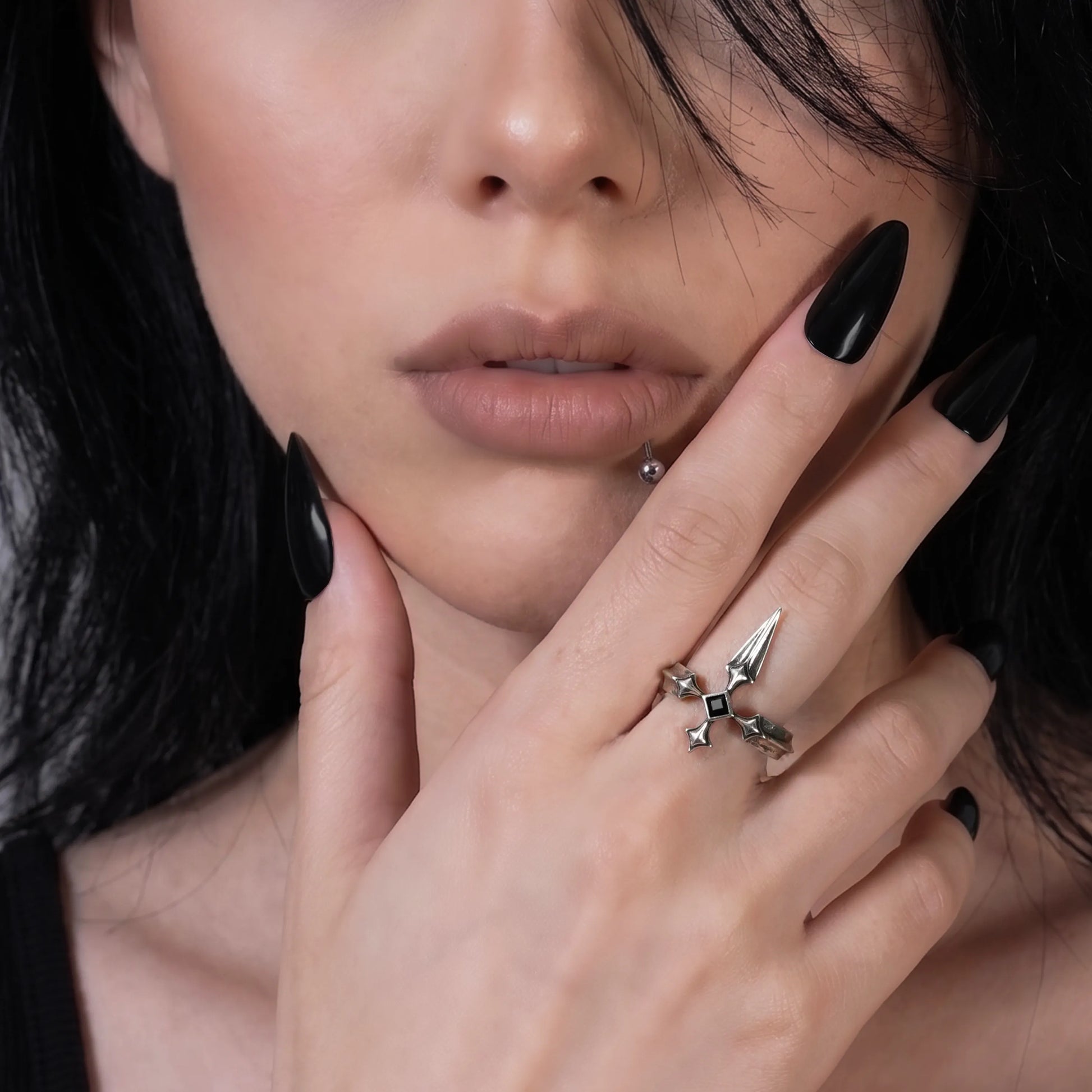 Vesper Blade Ring in silver worn on a raised hand near the lips in a close portrait with black nail polish.