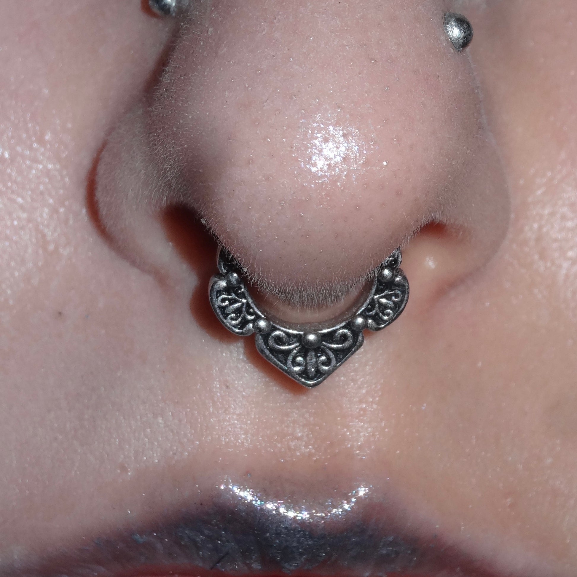 Silver-tone Victorian Bloom clicker worn in a septum piercing, close view of the engraved floral pattern