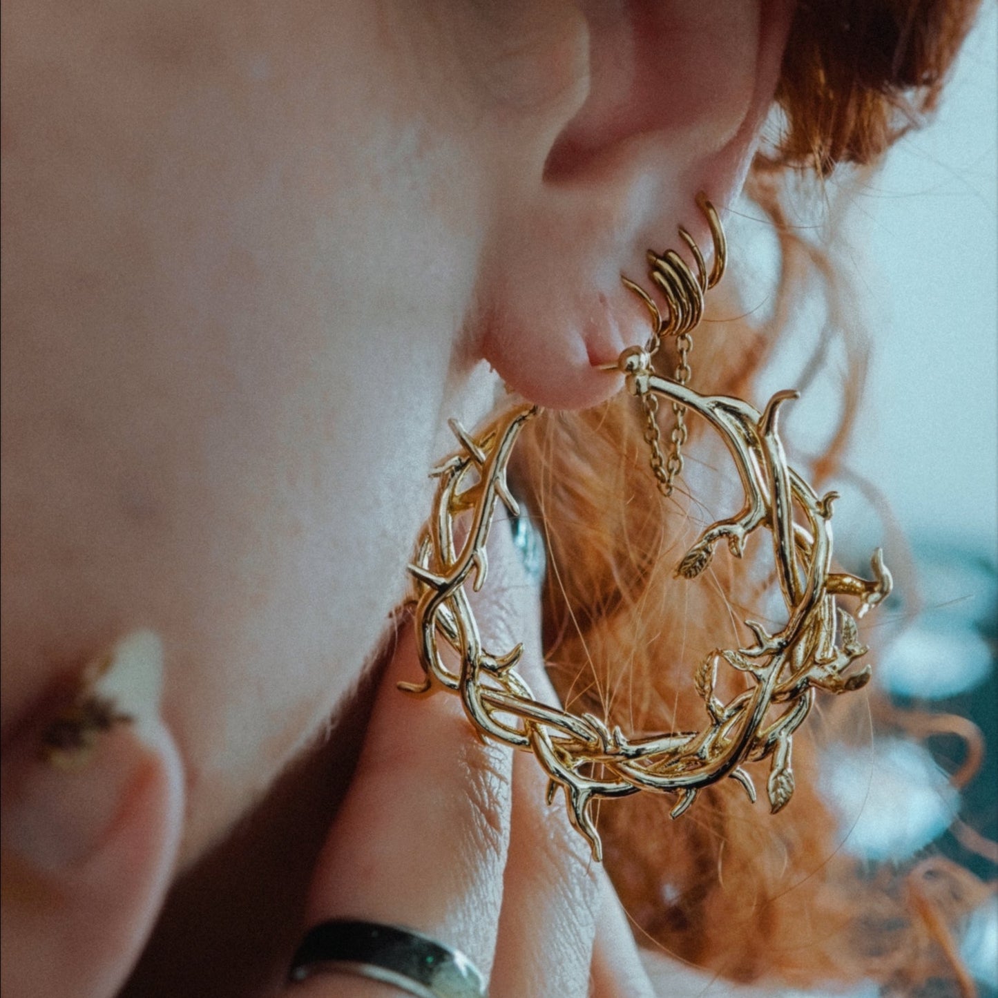 Close-up of a gold-tone vine and thorn hoop earring worn on a model's ear