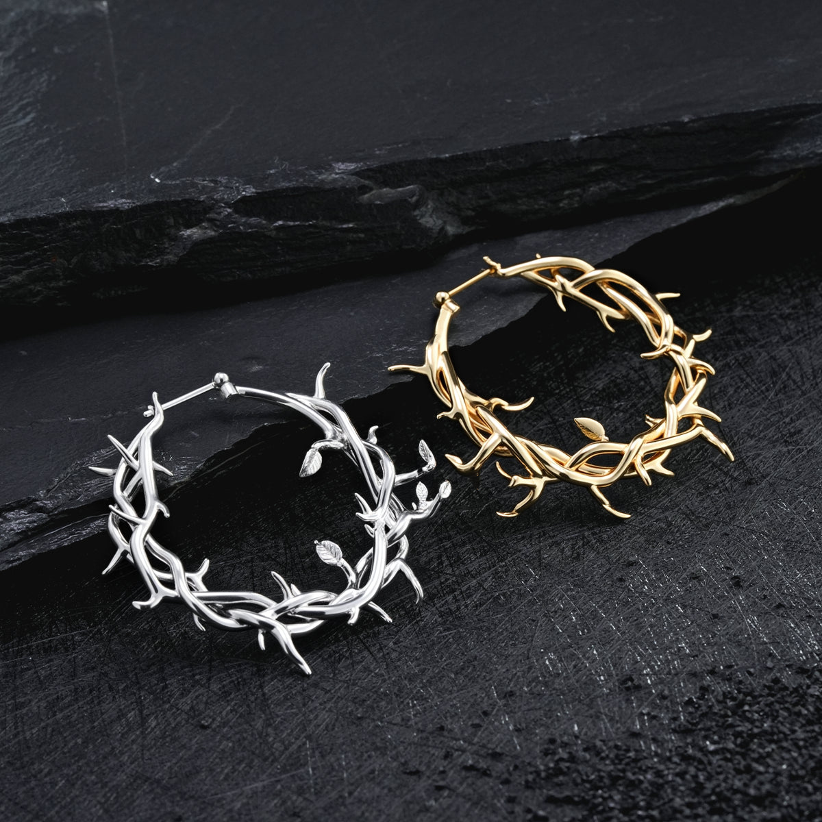 Silver and gold-tone Vine Whispers thorn hoop earrings displayed together on a textured black surface