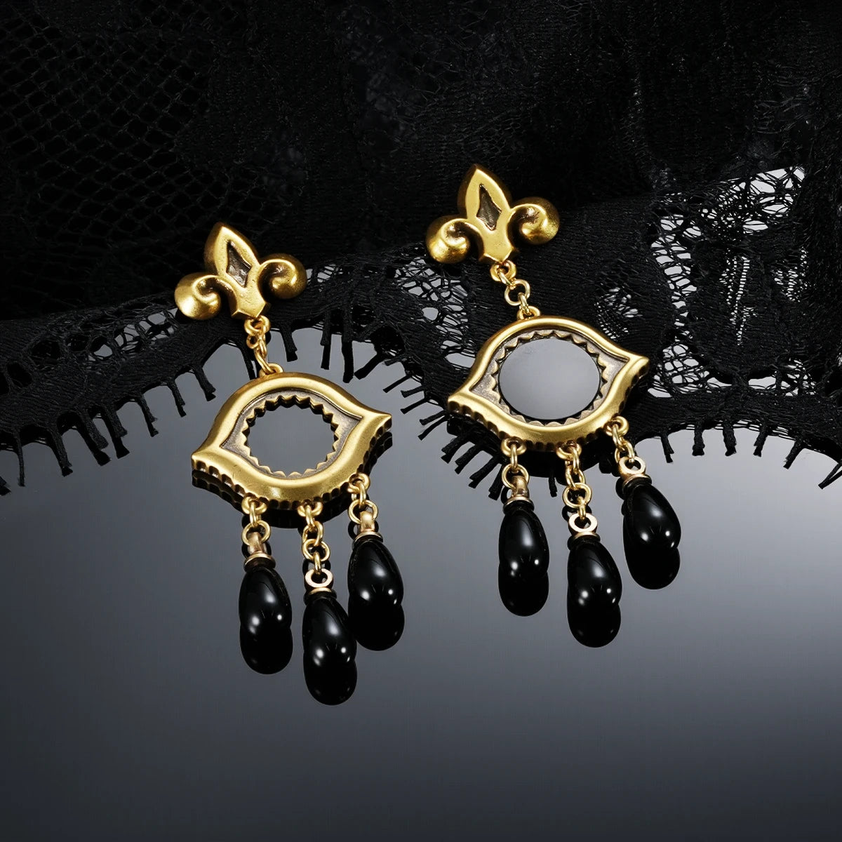 Gold-tone Votive Mirror Earrings displayed as a pair against black lace on a dark reflective surface.