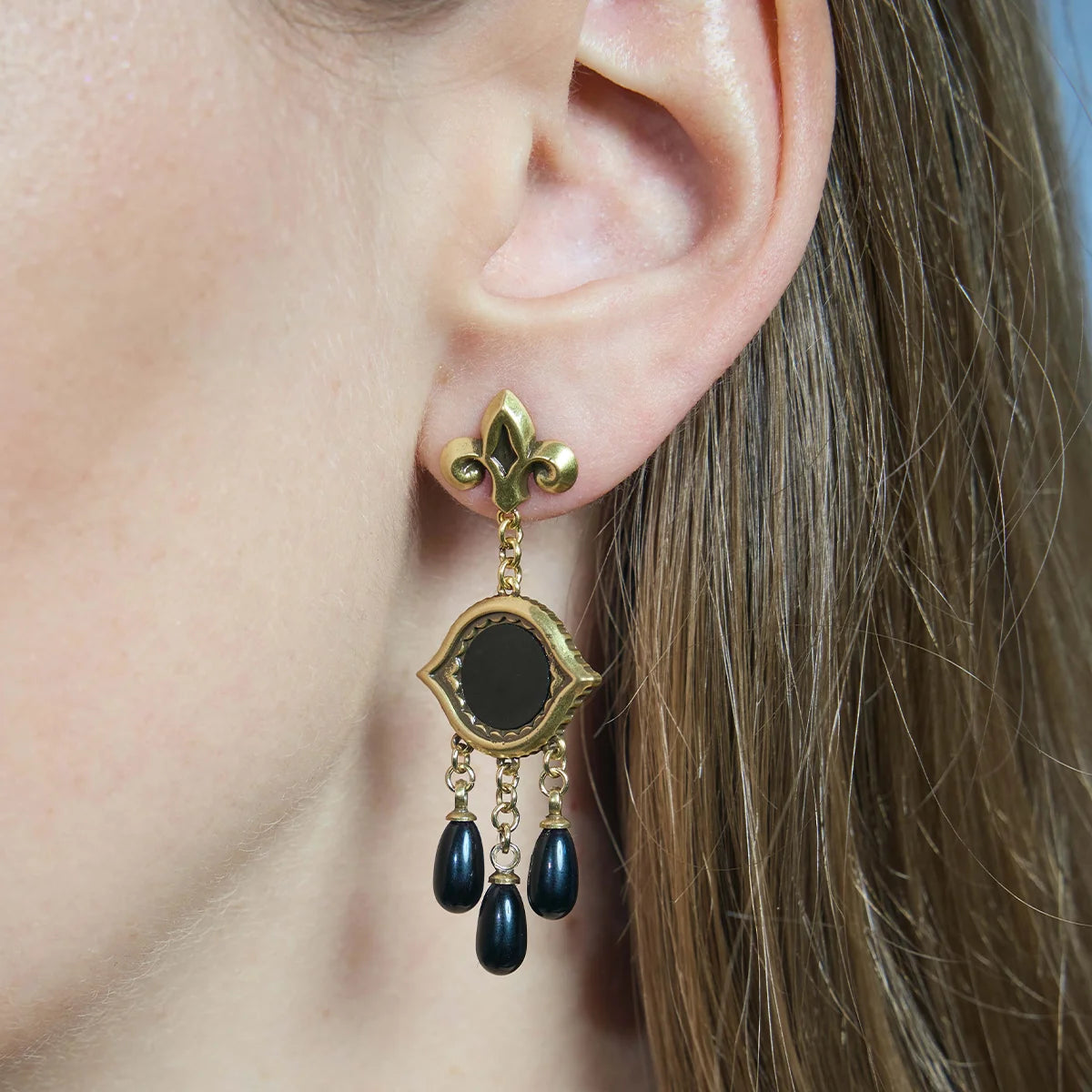 Close-up of a gold-tone Votive Mirror Earring worn from the side, featuring a round black obsidian center and three black drop accents.