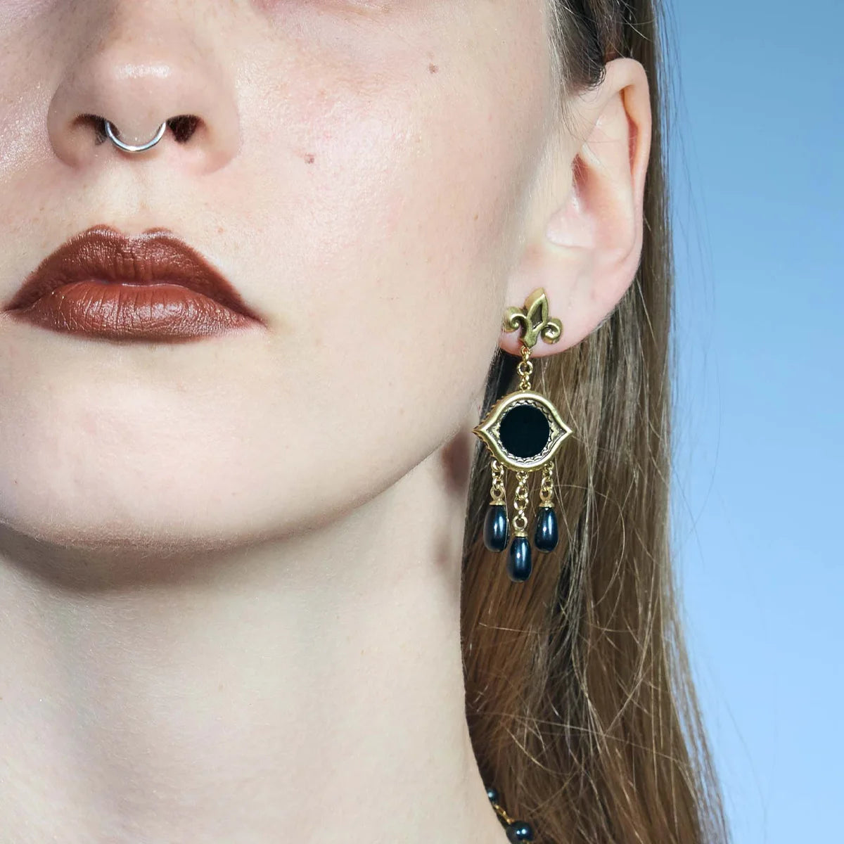 Front close-up of a gold-tone Votive Mirror Earring, highlighting the round black obsidian center and layered black drops.