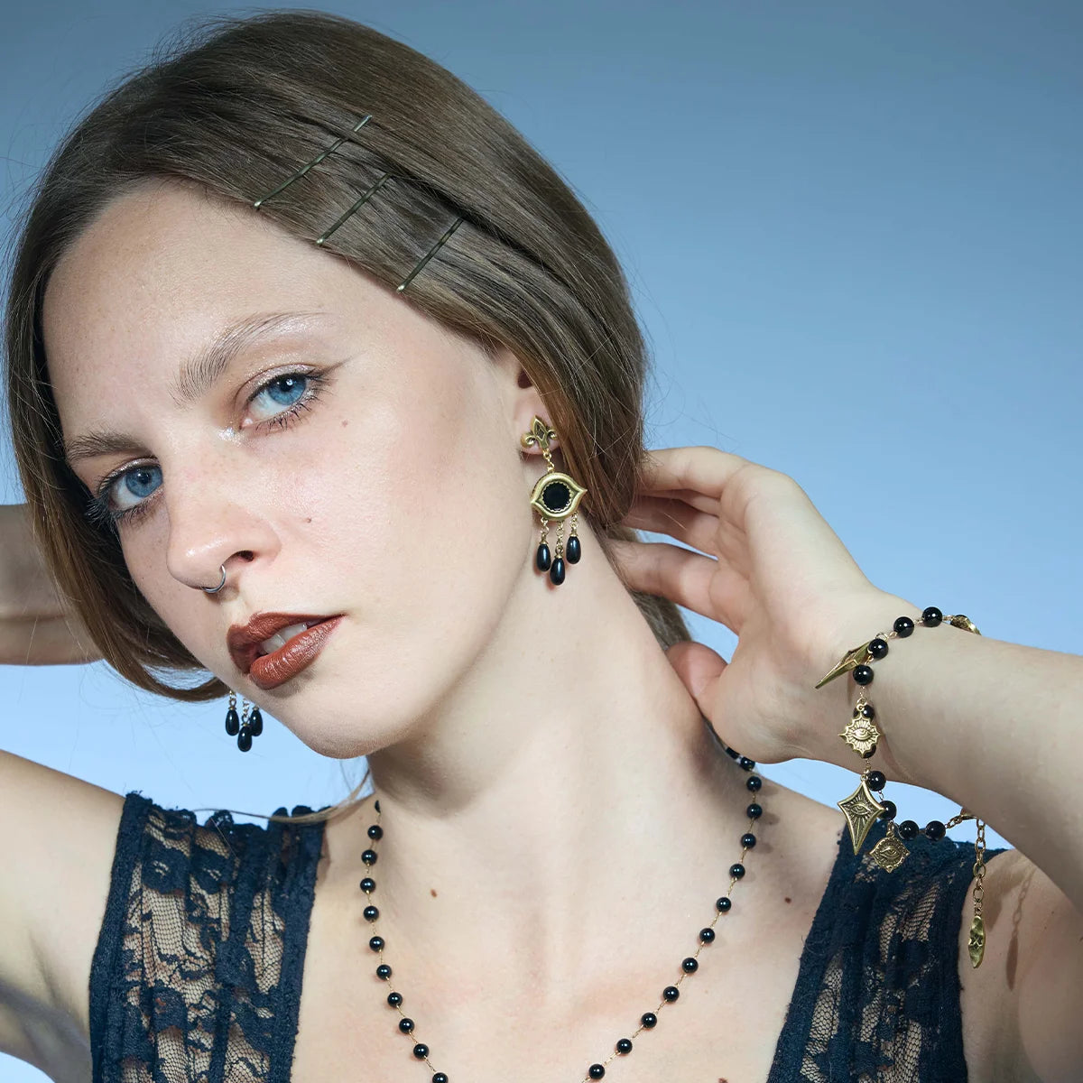 Three-quarter portrait showing gold-tone Votive Mirror Earrings with round black obsidian centers and layered black drop accents.
