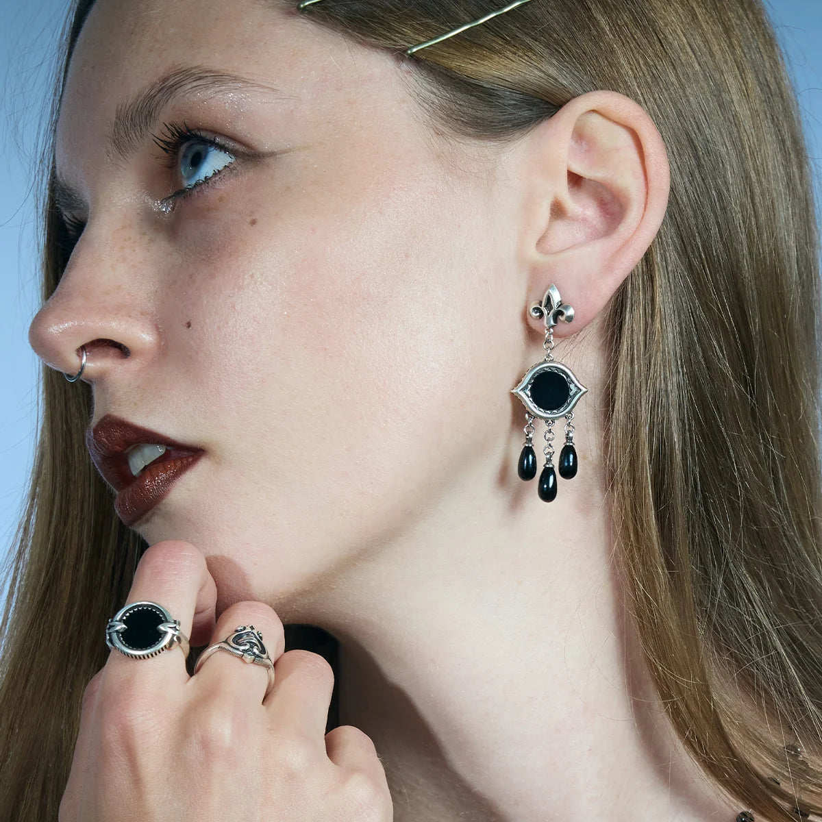 Side portrait showing antiqued silver-tone Votive Mirror Earrings with round black obsidian centers and three suspended black drops.
