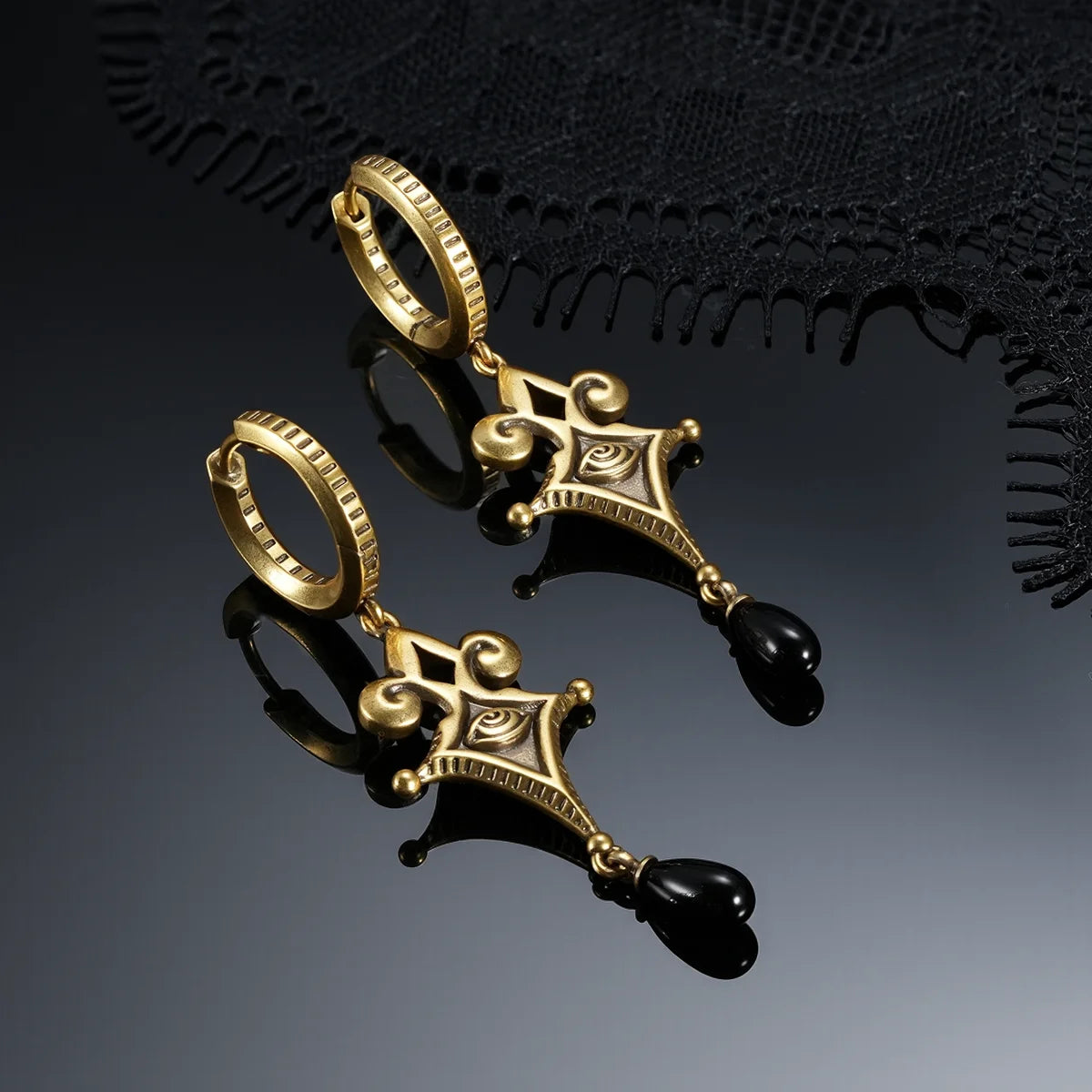Gold-tone Watcher’s Tear Earrings displayed from multiple angles against black lace on a dark reflective surface.