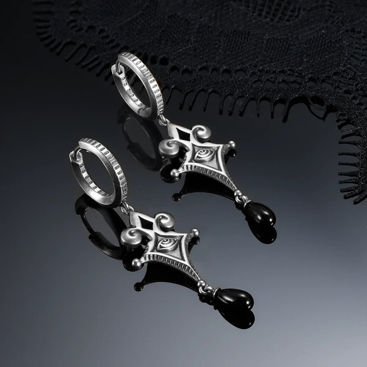 Antiqued silver-tone Watcher’s Tear Earrings displayed from multiple angles against black lace on a reflective surface.