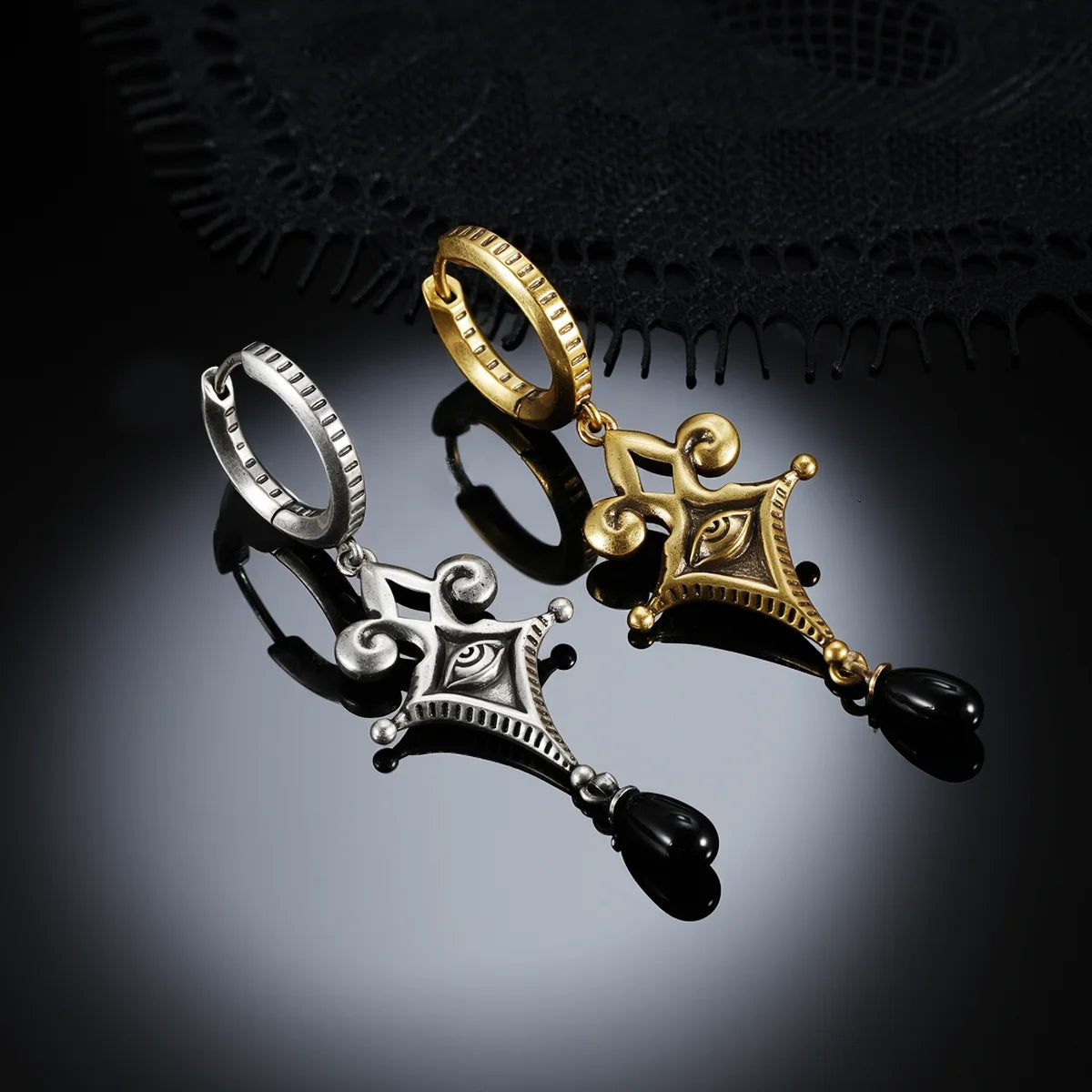 Antiqued silver- and gold-tone Watcher’s Tear Earrings displayed together against black lace on a dark reflective surface.