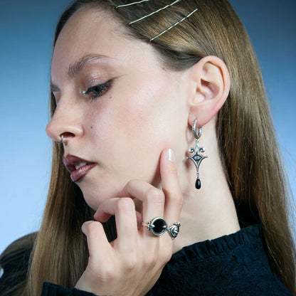 Side portrait of an antiqued silver-tone Watcher’s Tear Earring, highlighting the pointed ornamental frame and black teardrop drop.