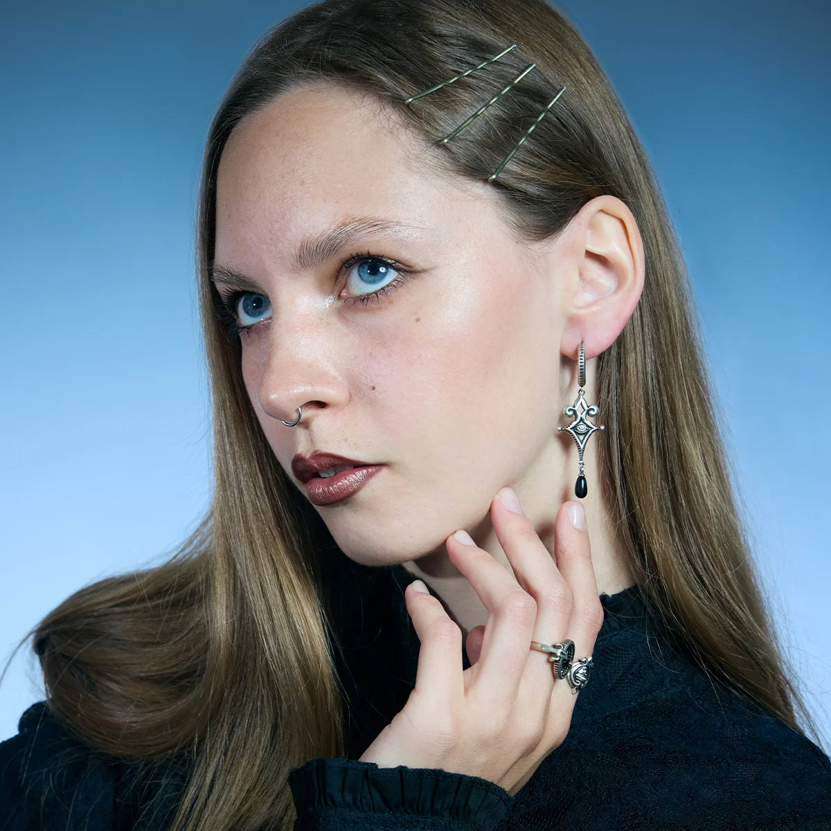 Antiqued silver-tone Watcher’s Tear Earrings worn in a styled portrait, showing engraved eye motifs and suspended black teardrop accents.