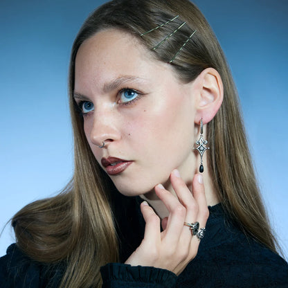Antiqued silver-tone Watcher’s Tear Earrings worn in a styled portrait, showing engraved eye motifs and suspended black teardrop accents.