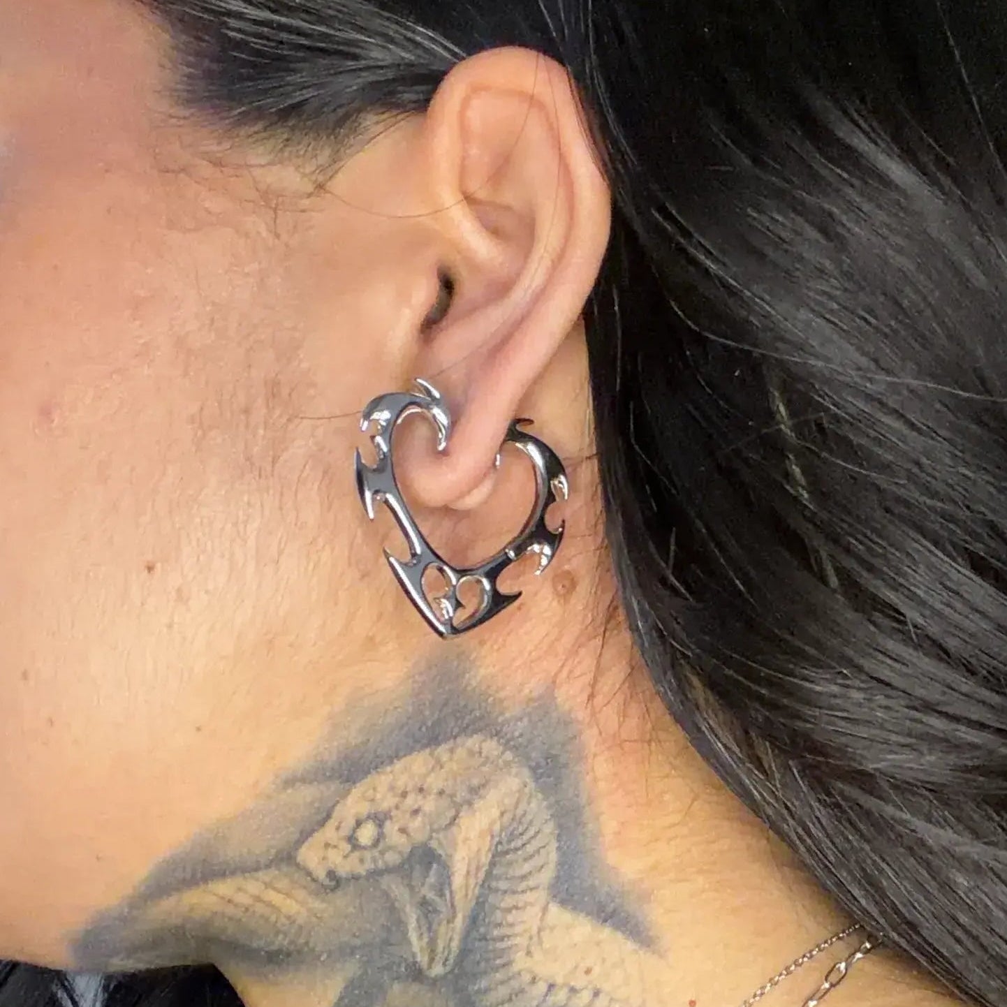 wild heart earrings shown on a model in side view, featuring silver heart-shaped hoop earrings with an open gothic frame design