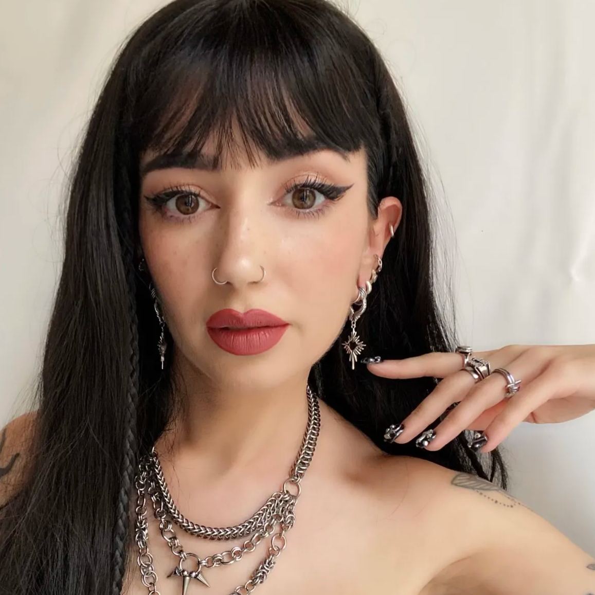 Winged Heartburst Earrings in 925 sterling silver, worn in a front portrait with black bangs, layered necklaces, and silver r