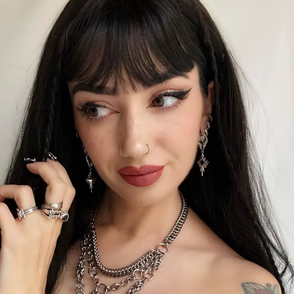 Winged Heartburst Earrings in 925 sterling silver, worn in a three-quarter portrait with black bangs, facial piercings, and s