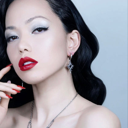 Winged Heartburst Earrings in 925 sterling silver, worn in a polished portrait with black waves, winged eyeliner, and red lip