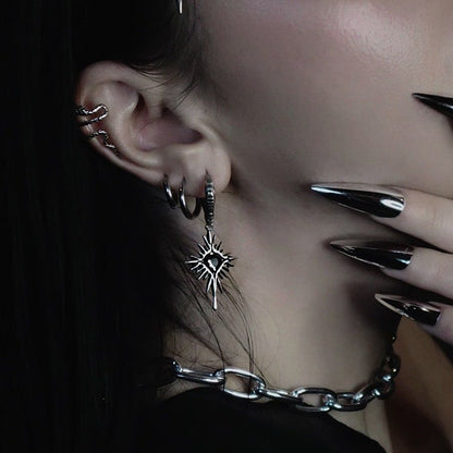 Winged Heartburst Earrings in 925 sterling silver, worn in a dark-haired ear stack with small hoops and an ear cuff, beside g