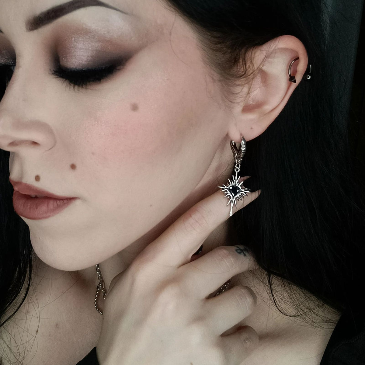 Winged Heartburst Earrings in 925 sterling silver, worn in an eyes-closed side portrait with dark hair and a hand under the c