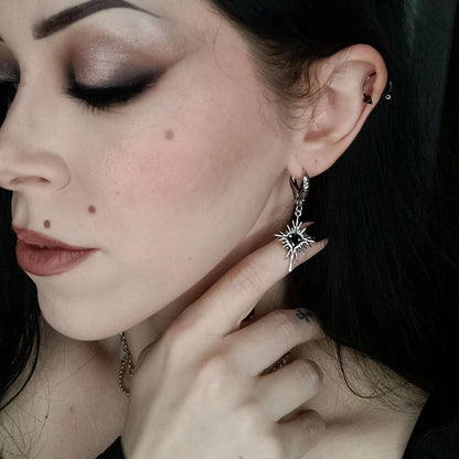 Winged Heartburst Earrings in 925 sterling silver, worn in an eyes-closed side portrait with dark hair and a hand under the c