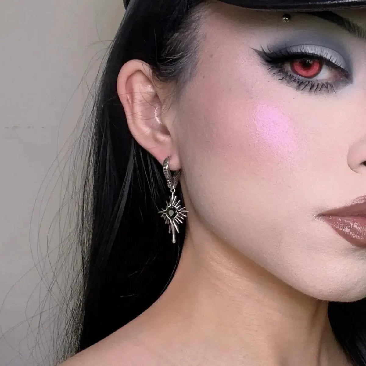 Winged Heartburst Earrings in 925 sterling silver, worn in a dramatic close-up with a red contact lens, graphic eye makeup, a