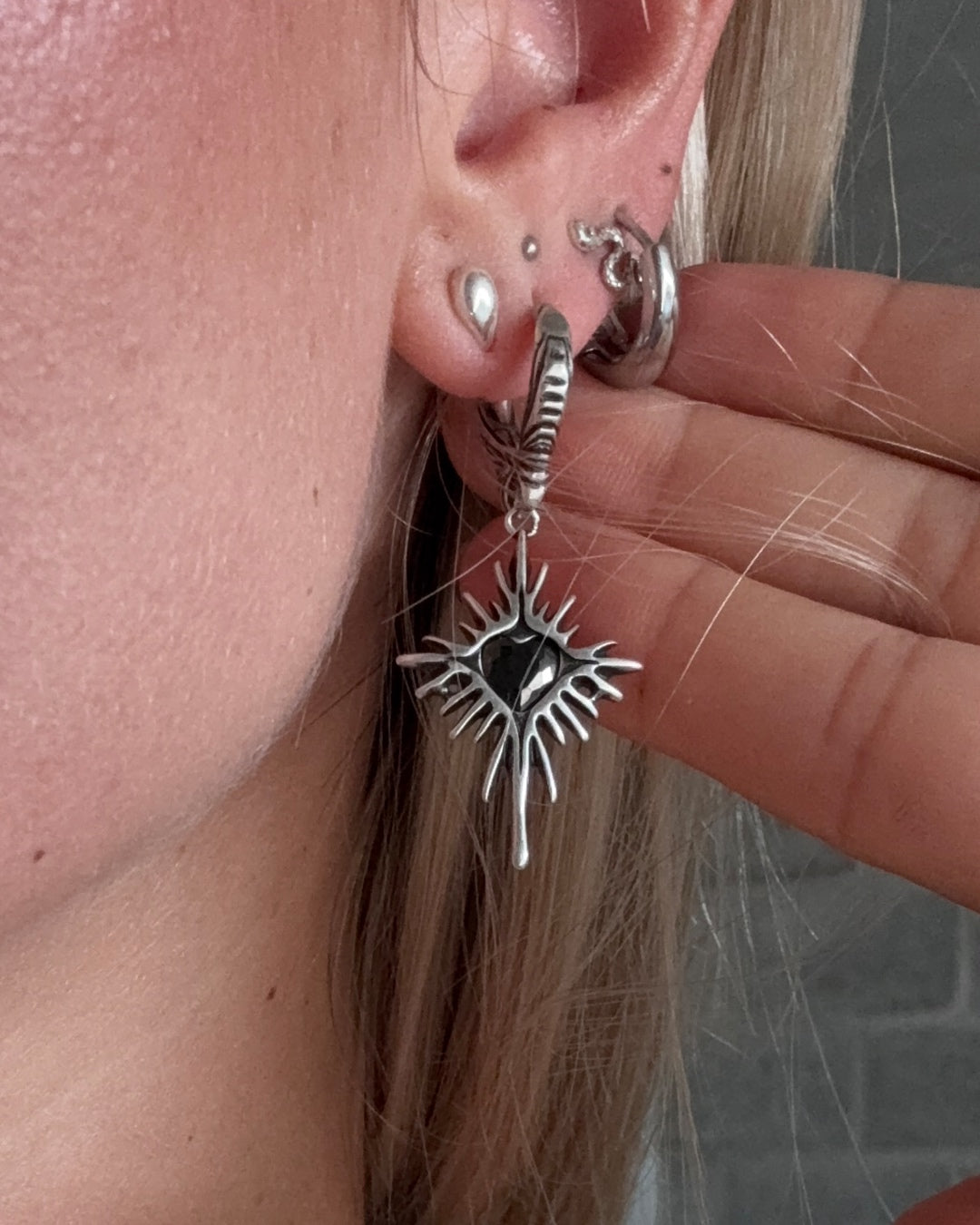 Silver Winged Heartburst Earring with black centre worn on an ear.