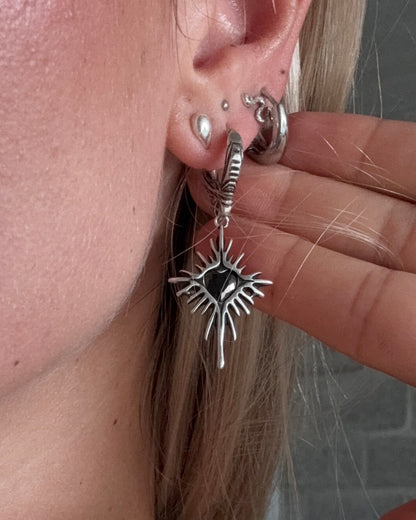 Silver Winged Heartburst Earring with black centre worn on an ear.