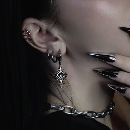 Starburst charm earring with black stone worn among multiple hoops and an ear cuff on a dark-haired model