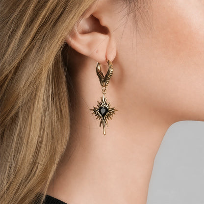 Gold-tone Winged Heartburst hoop earring worn on an earlobe, with a black heart and radiating spikes