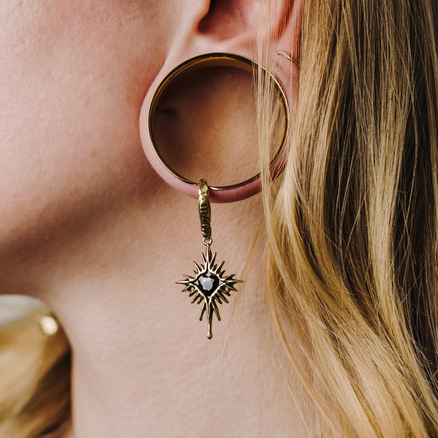 Gold-tone Winged Heartburst earring hanging through a large circular ear plug