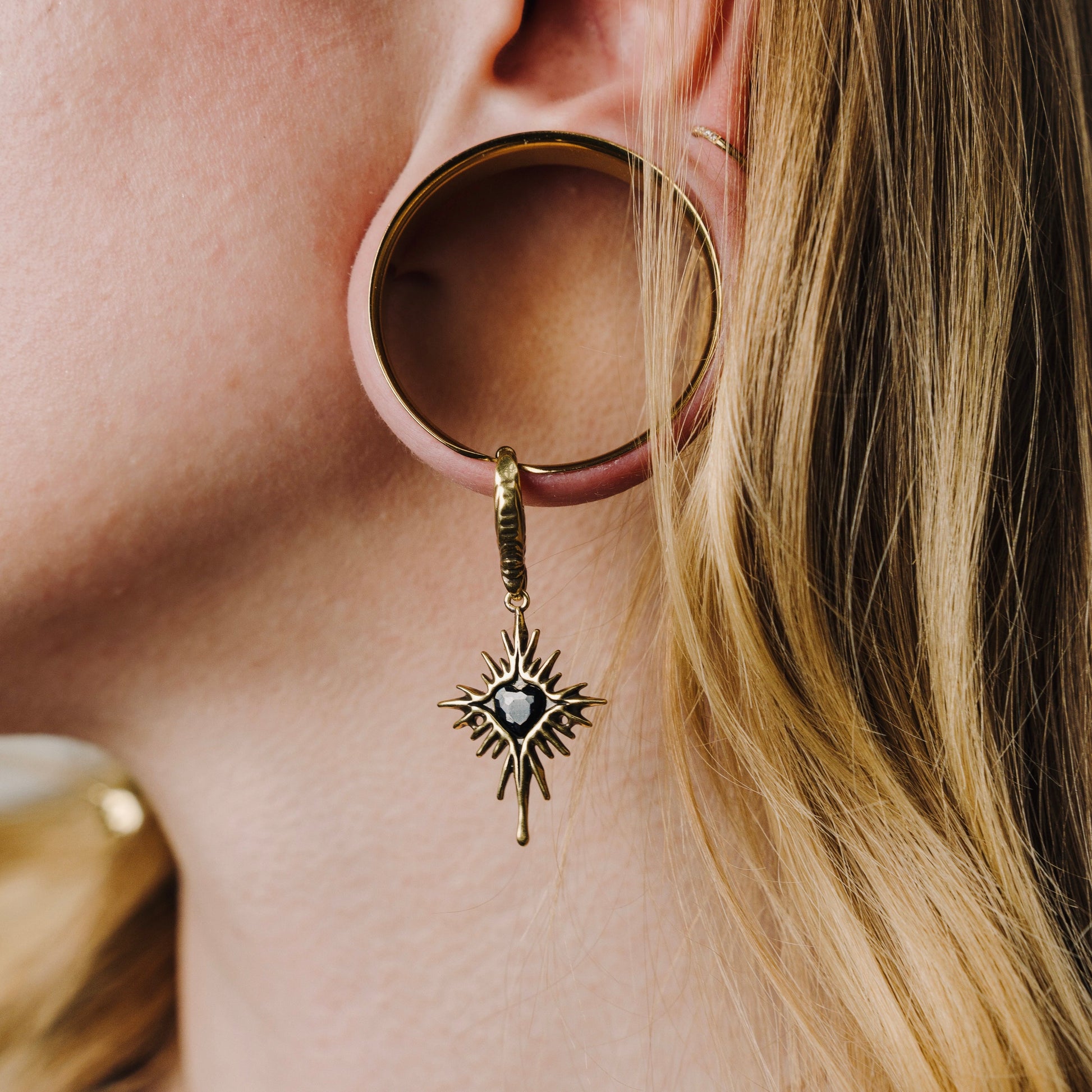 Gold-tone Winged Heartburst earring hanging through a large circular ear plug