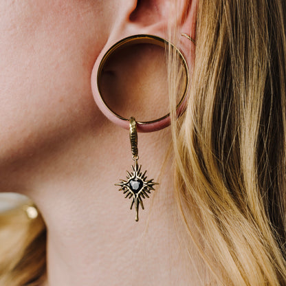 Gold-tone Winged Heartburst earring hanging through a large circular ear plug