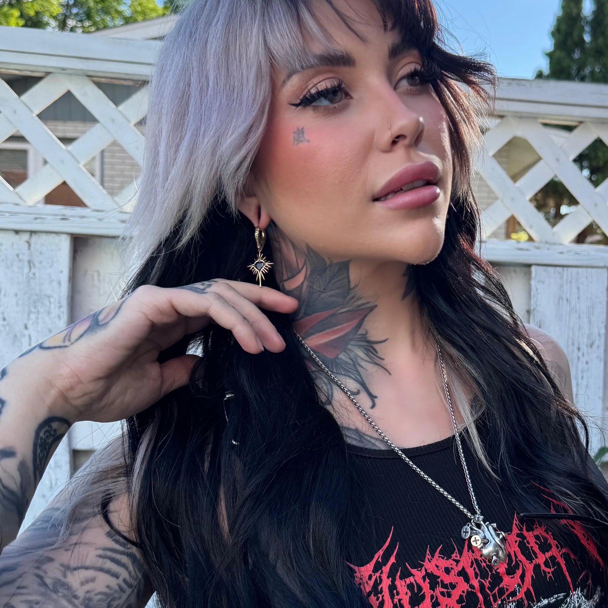 Model wearing Winged Heartburst Earrings outdoors, showcasing silver winged heartburst drop earrings in a gothic and alternative fashion styling.