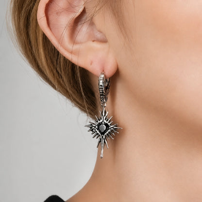 Silver-tone starburst drop earring with a black center stone, worn on a hoop, close-up side view