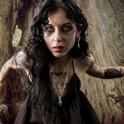 Wrapped Relic Earrings in 925 sterling silver, worn in a dark woodland portrait beside a tree trunk with layered necklaces an