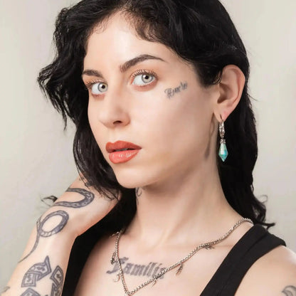 Wrapped Relic Earrings in 925 sterling silver, worn in a three-quarter portrait with visible tattoos, layered necklaces, and 