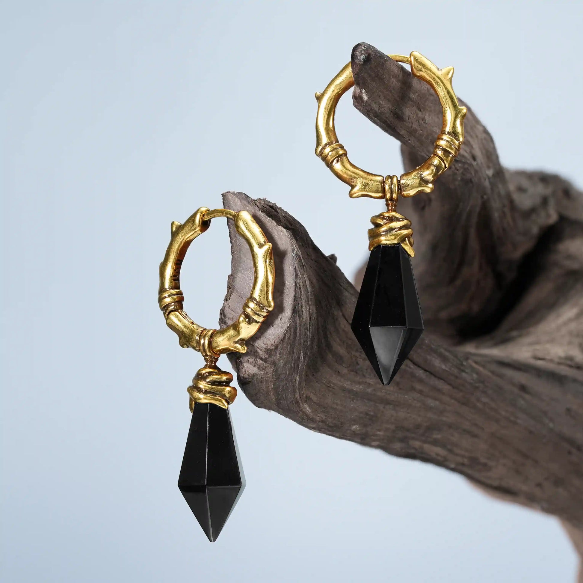 Gold Wrapped Relic Earrings with black obsidian drops displayed on weathered wood