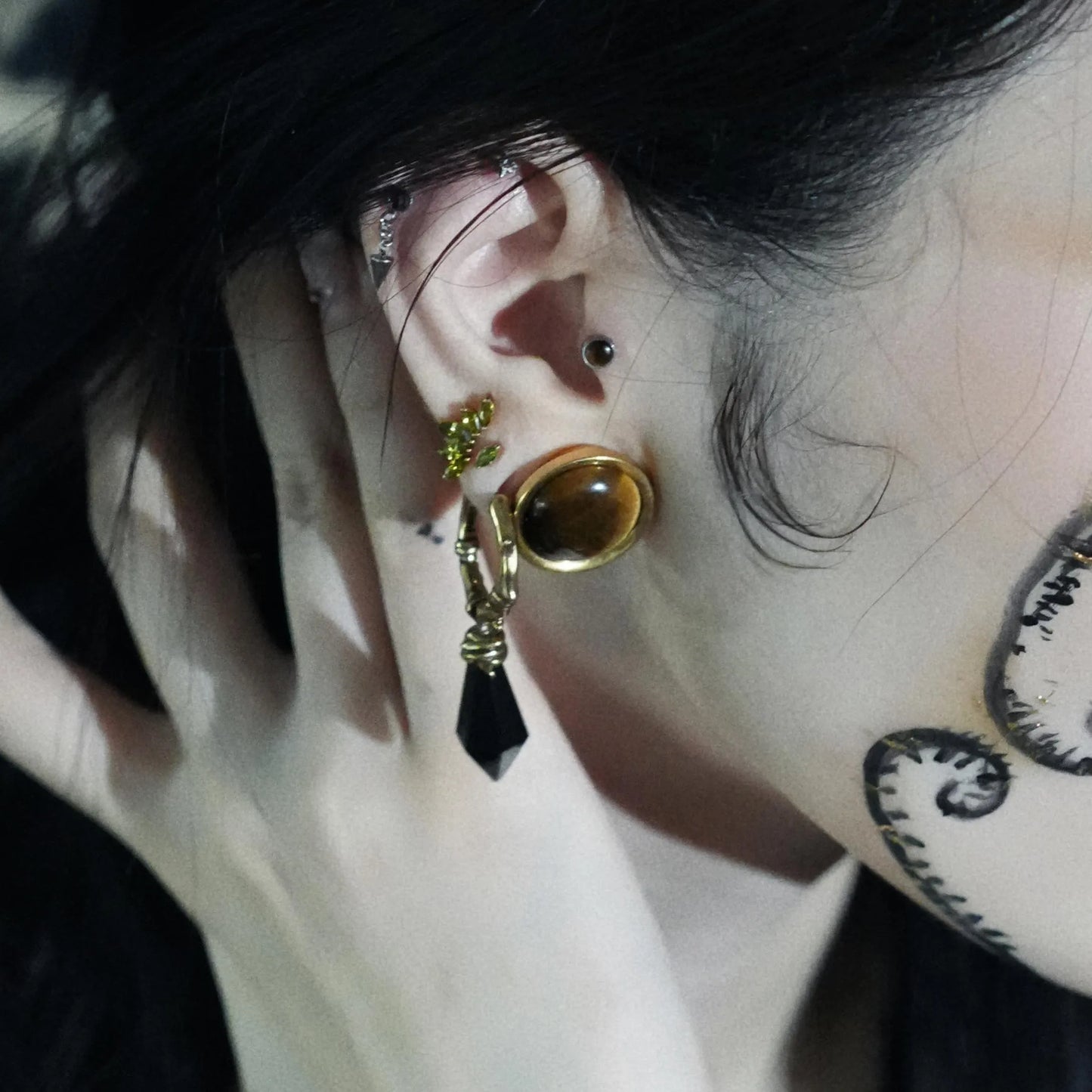Model wearing the gold Wrapped Relic Earrings with black obsidian dagger drops, layered with bold gothic ear jewelry and dark forest styling.
