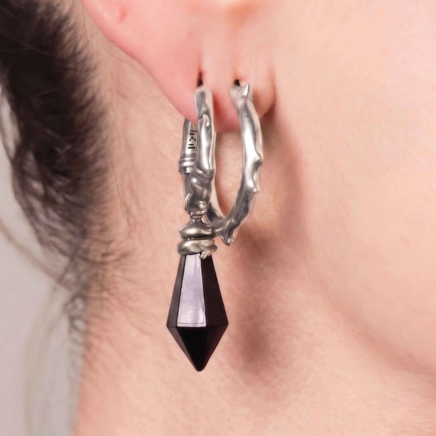 Model wearing the silver Wrapped Relic Earrings with black obsidian dagger drops, showing the sharp gothic silhouette and relic-inspired hoop design.