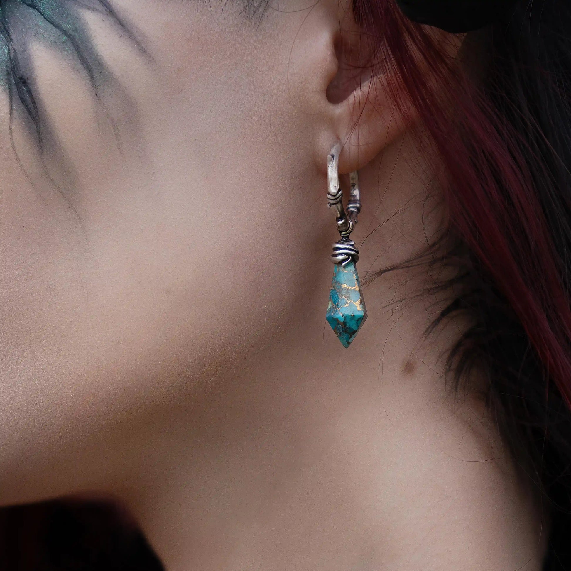 Model wearing the silver Wrapped Relic Earrings with turquoise dagger drops, showing the relic-inspired hoop design in dark gothic styling.